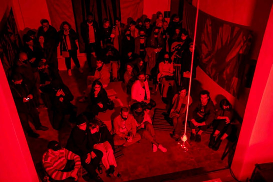 Audience in a red-lit installation at 2LAB
